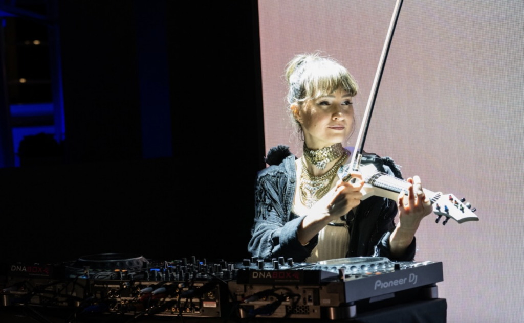 Alfiya Glow playing electric violin with DJ table setup