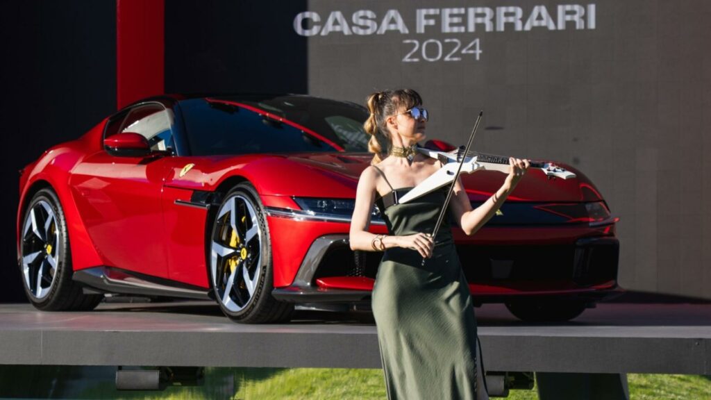 Alfiya Glow playing electric violin outside Casa Ferrari with a red Ferrari in the back